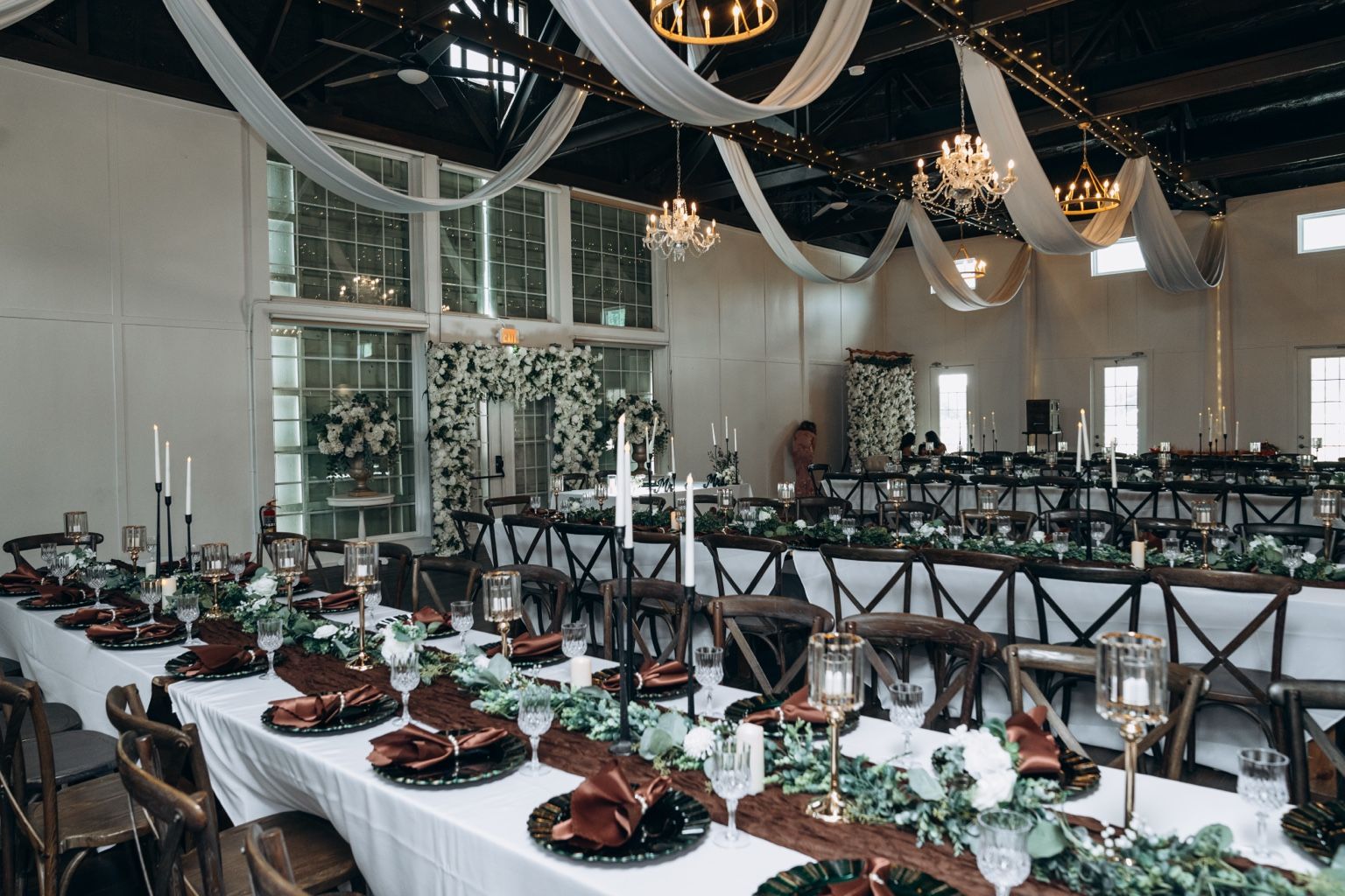 A wide reception hall with long banquet tables, draping and chandeliers